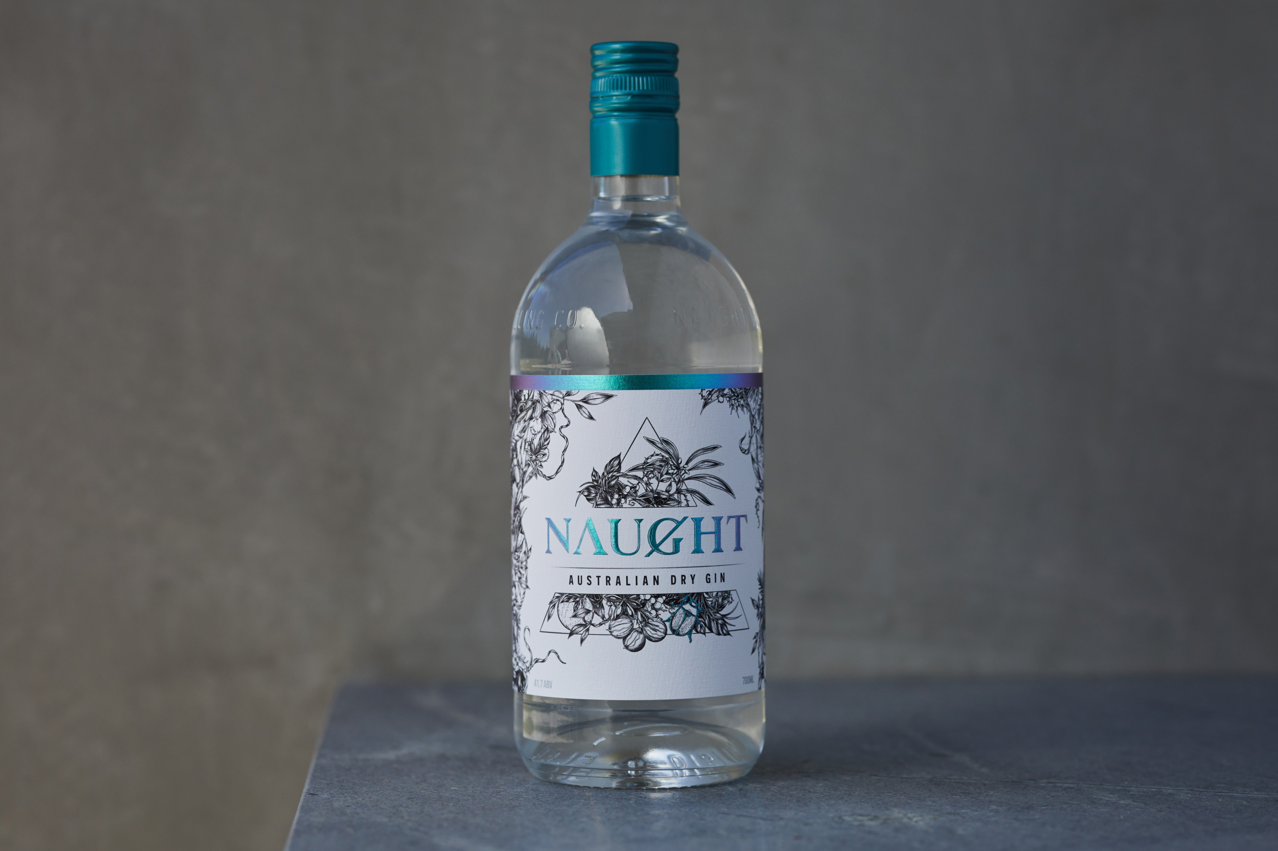 Bottle of Naught Australian Dry Gin with an elegant label design, featuring botanical illustrations, set against a minimalist gray background, highlighting its premium and sophisticated branding.