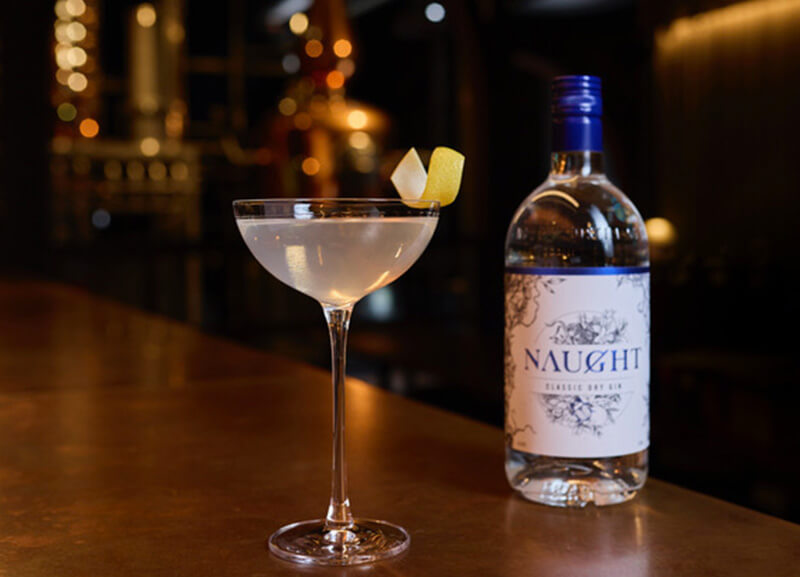 A Naught classic dry martini placed on the cooper bar next to a bottle of Naught Classic Dry Gin