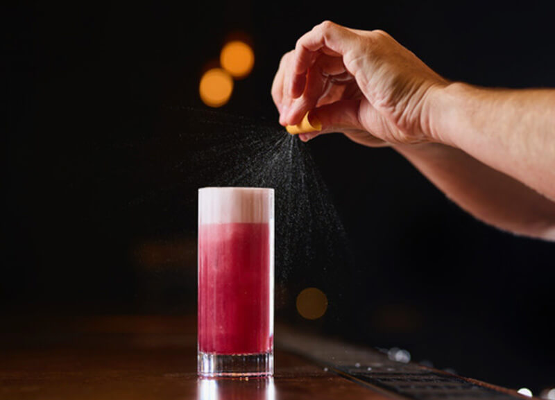 a bartender squirts an orange rind onto the naught shiraz gin fizz cocktail
